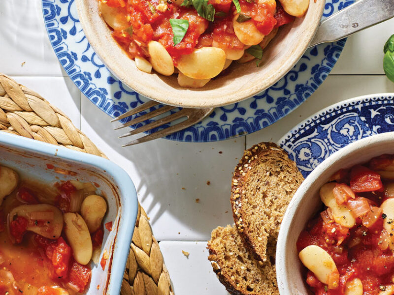 Gigantes Plaki: Greek Lima Beans with Stewed Tomatoes in white bowls placed on white and blue china plates, served with a side of dark bread