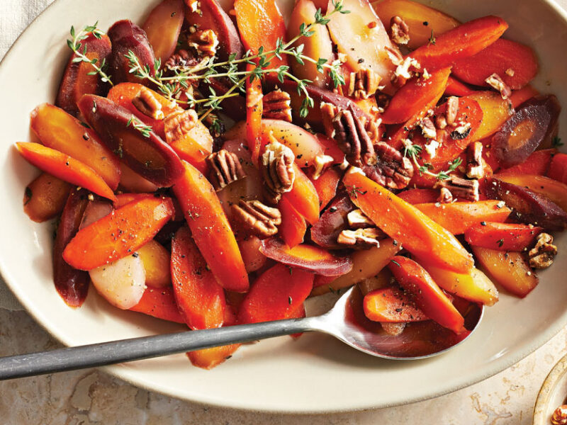 Maple-Glazed Carrots with Thyme in a white oval dish with a metal serving spoon