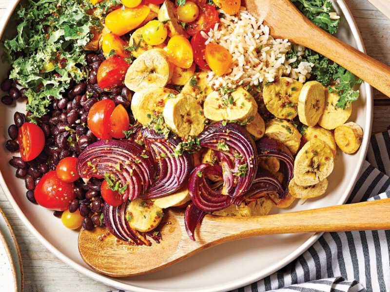 Mojo-Seasoned Plantain Salad with Black Beans and Rice in a white ceramic bowl with wooden serving spoons