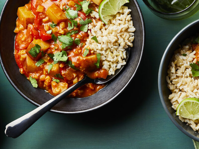 Vegan Red Curry with Cauliflower and Potatoes in gray ceramic bowls with metal spoons against a blue countertop