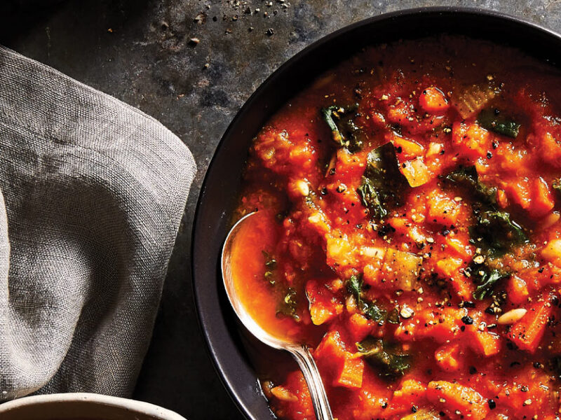 Carrot Ginger Soup with Orzo and Kale in a black bowl with a metal spoon against a gray countertop
