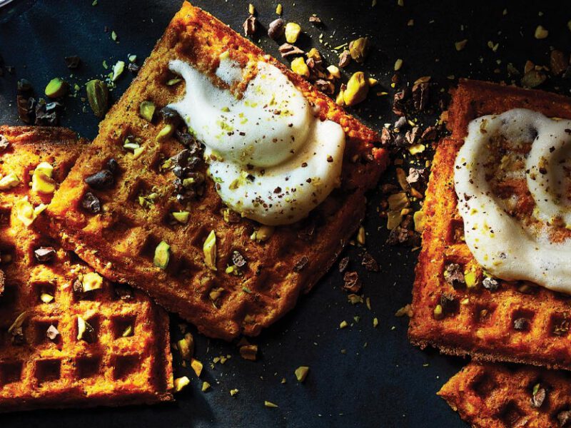 Sweet Potato Dessert Waffles topped with crushed nuts and whipped cream placed on a dark background