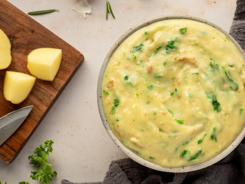 Good Garlicky Mashed Potatoes in a bowl next to a cutting board with potato wedges