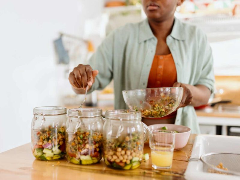 African American woman spooning chickpeas into mason jars holding meal prep salads