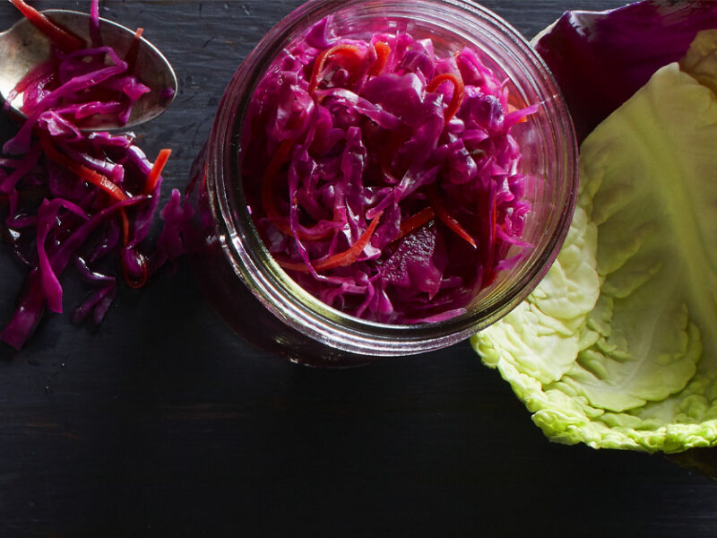 Spicy Red Cabbage Sauerkraut in a mason jar next to leaves of red and green cabbage