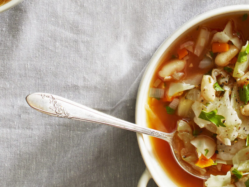 Green Cabbage and White Bean Soup in white ceramic bowls with a metal spoon against a gray cloth background