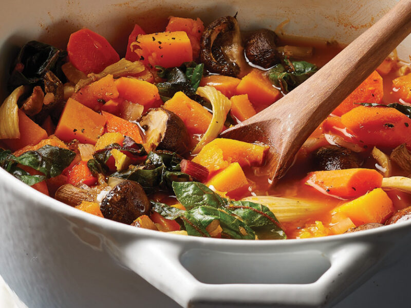 Roasted Kabocha Squash and Veggie Stew in a white Dutch oven with a wooden stirring spoon