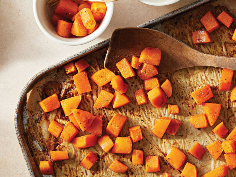 Butternut Squash with Orange Glaze on a baking sheet with a wooden spatula