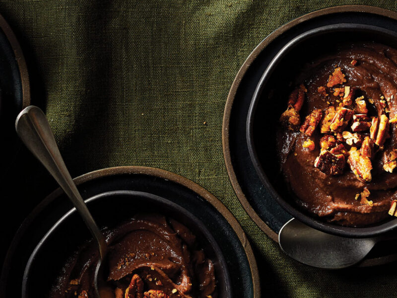 Creamy Sweet Potato Pudding topped with pecans in dark gray ceramic bowls against a green linen tablecloth