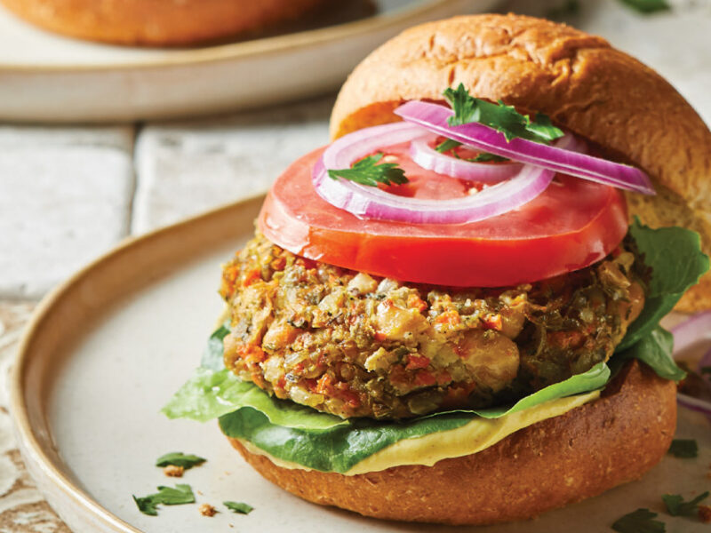 Tuscan White Bean Burgers topped with onion and tomato and on white ceramic plate