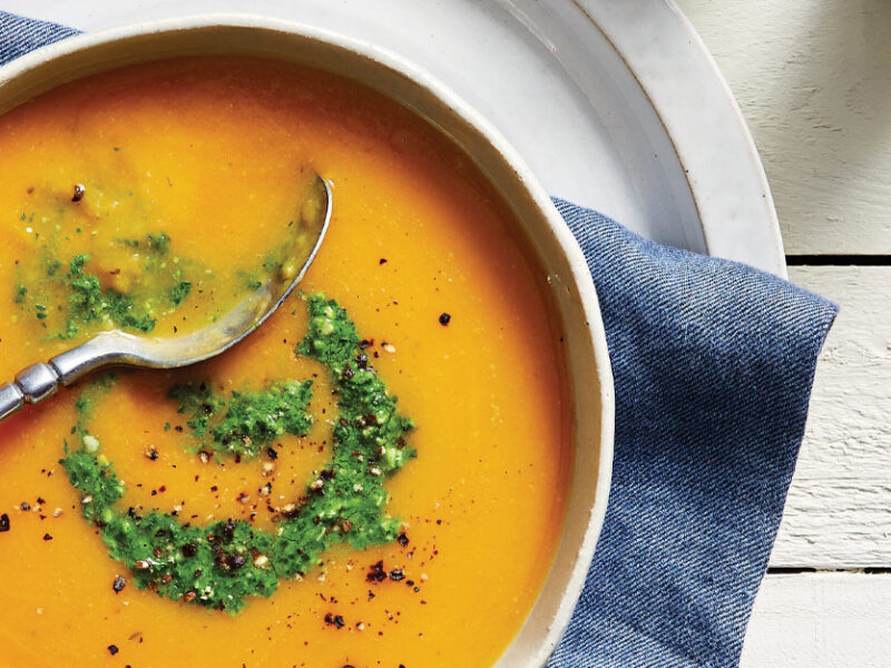Butternut Bisque with Parsley Pistou in a white ceramic bowl resting on a blue cloth napkin