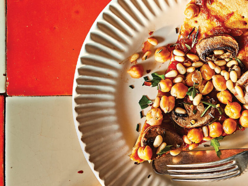Vegan Mushroom and Chickpea Pizza with Rosemary on a white plate against a red and white checkerboard tile background