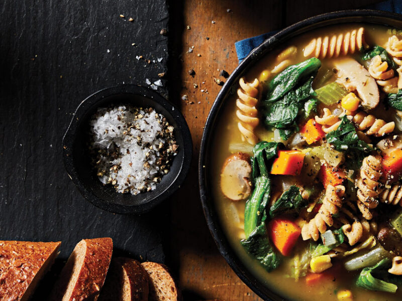 Creamy Vegetable Soup with Escarole in a black bowl next to a loaf of bread and a small bowl of salt