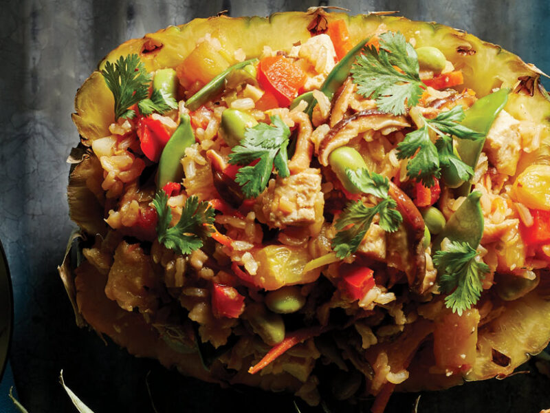 Thai Pineapple Fried Rice served in a hollowed out pineapple half against a dark gray background