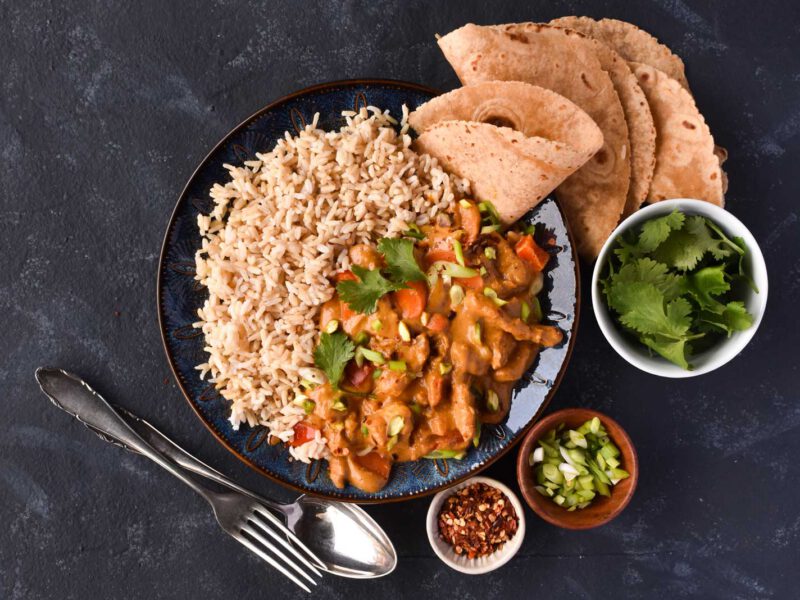 Vegetable Tikka Masala in a large black bowl surrounded by small bowls of cilantro, scallions, and chili flakes