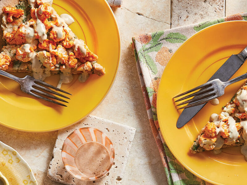 Buffalo Cauliflower Pizza on orange plates with metal knives and forks