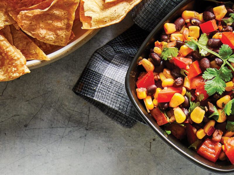 Spicy Black Bean Salsa in a black bowl with a side of tortilla chips
