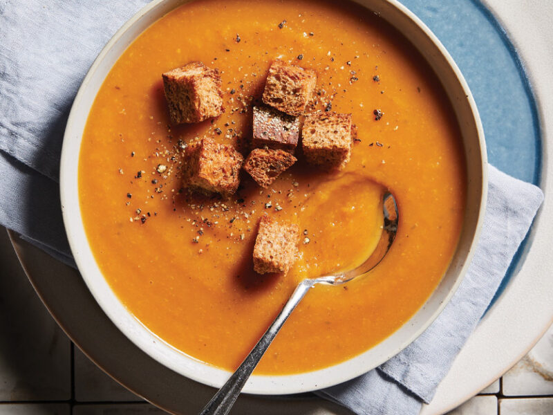 Root Vegetable Bisque with Whole Grain Croutons in a white bowl with a metal spoon