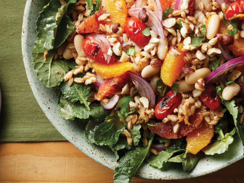 Orange Farro Salad with Pan-Roasted Tomatoes on a light gray plate with a small bowl of mustard dressing to the left side