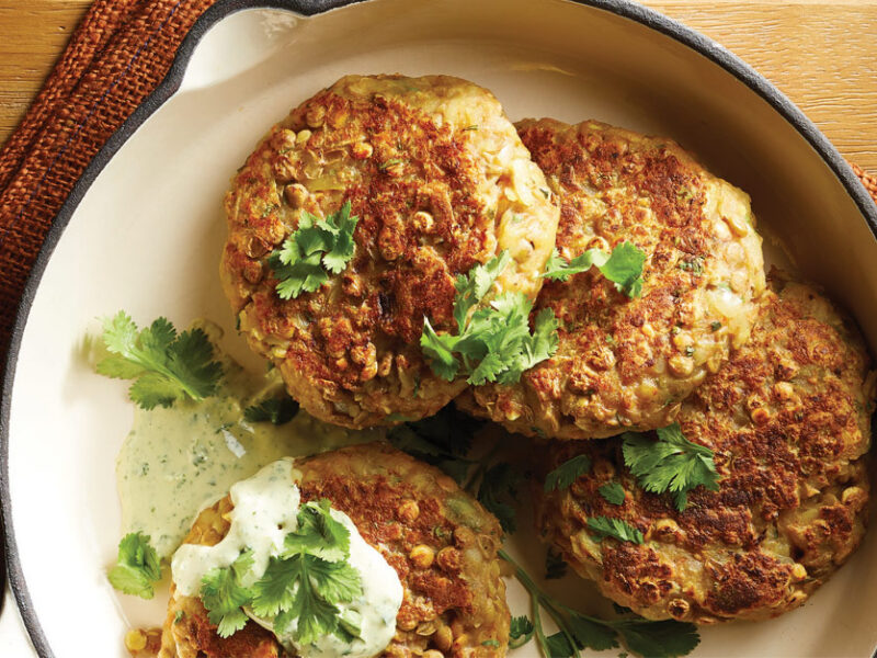 Hash Brown Patties with Green Tahini Sauce and fresh cialntro leaves in a white ceramic bowl sitting on an orange cloth napkin