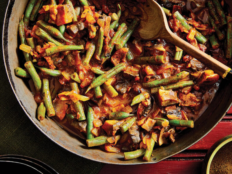 Inguday Tibs (Spicy Ethiopian Mushrooms) in a large metla pot with a wooden spoon against a red wooden background