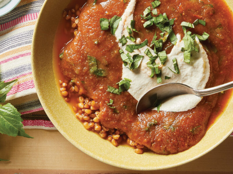 Roasted Tomato and Eggplant Soup in a yellow ceramic bowl with a metal spoon dipped into the soup