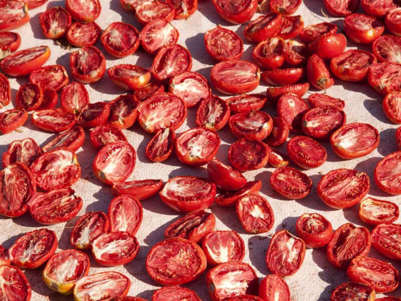 dozens of halved tomatoes lay out in the sun becoming sun-dried tomatoes