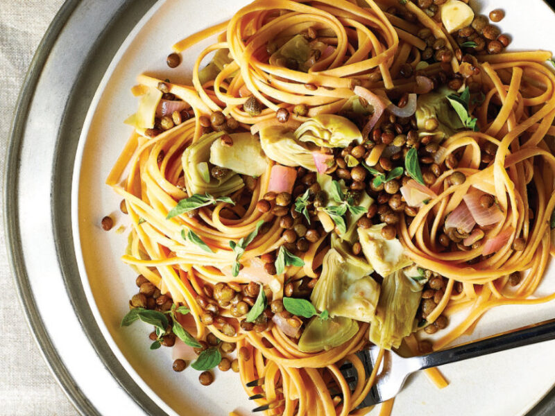 Linguine with Artichokes and Lentils on a white plate with a fork on the plate, covered in linguine