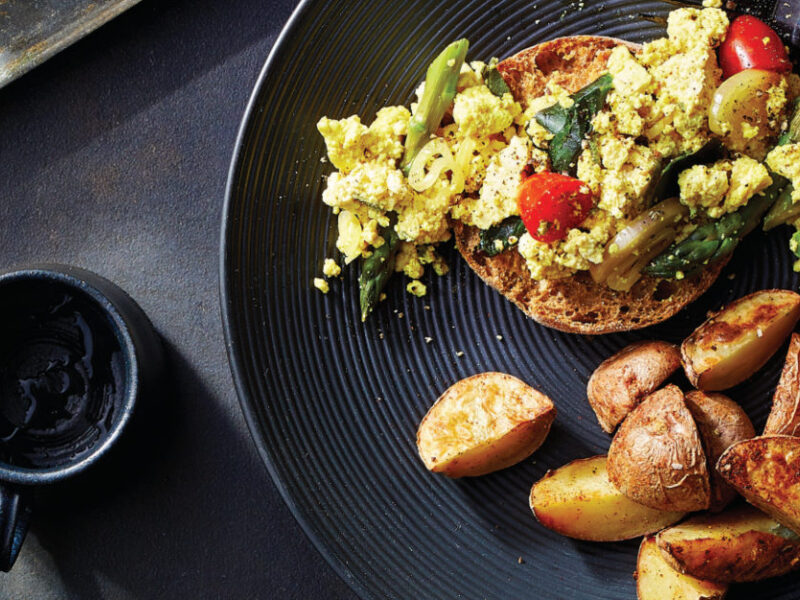 Tofu Veggie Scramble with Roasted Potatoes on a black plate on a dark grey background
