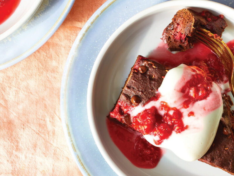 Raspberry Chocolate Cake drizzle with Aquafaba Whipped Cream and fresh raspberries on a pale blue plate on an orange table cloth