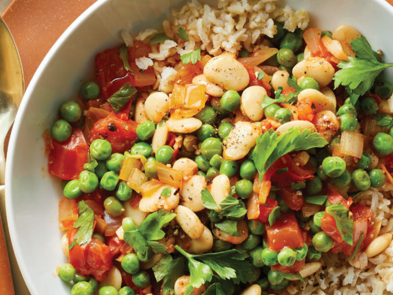 Spanish-Style Fava Beans in a white bowl sitting on a brown plate with a spoon on the side