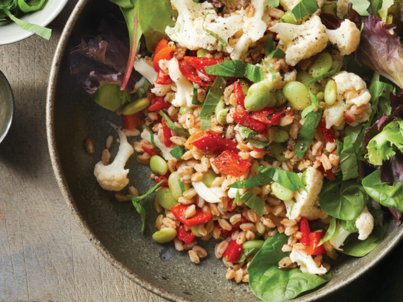 Pickled Cauliflower and Farro Salad in a brown earthy serving bowl on a wooden chopping board next to a small bowl of crushed red pepper