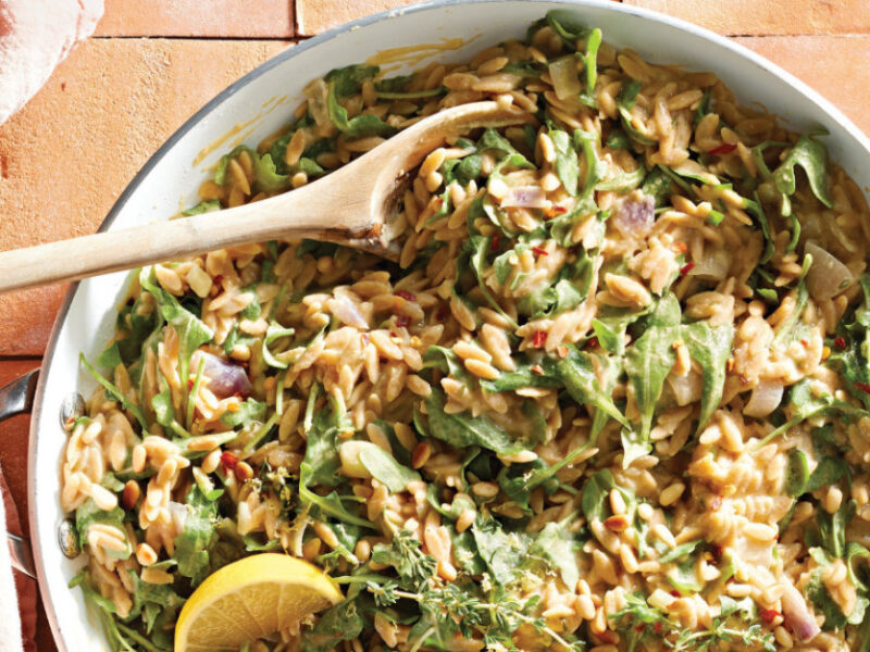 Whole Wheat Orzo and Arugula Skillet Supper in a white skillet with a wooden spoon