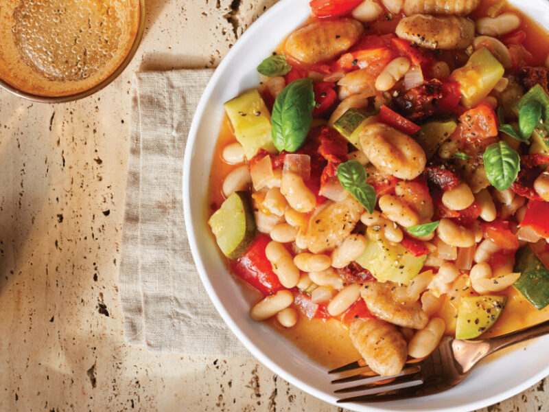 Quick Gnocchi with Zucchini, Tomato, and White Beans in a white pasta bowl on a folded cloth napkin on a light wooden table top