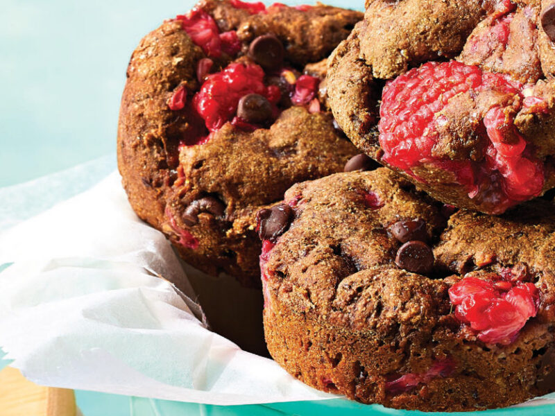Closeup of three Chocolate Raspberry Brownie Bites on a pale blue background in a bowl with a white napkin