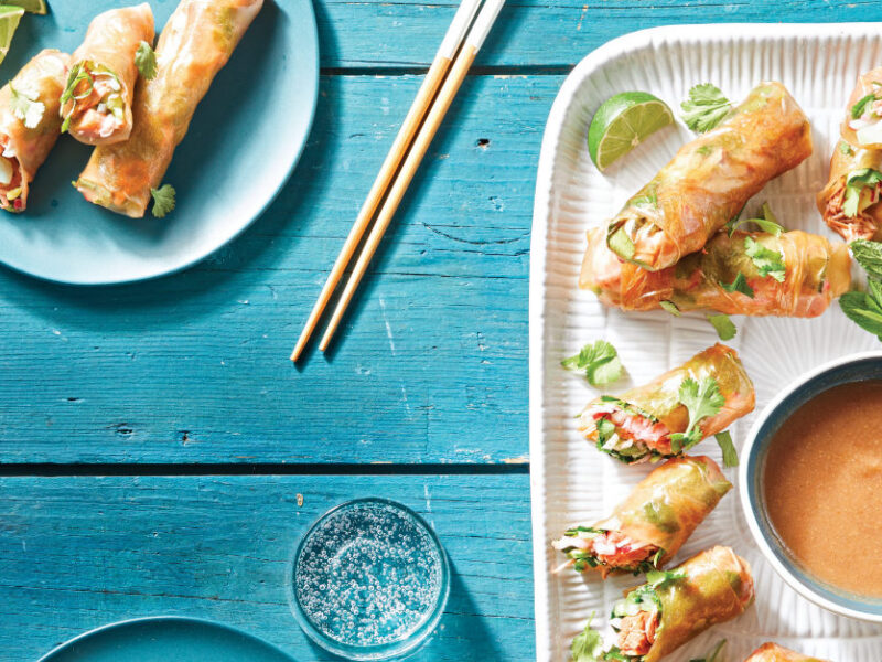 Jackfruit Spring Rolls on a white rectangular serving plate with a small bowl of Sweet-and-Sour Dipping Sauce on a blue wooden table with a smaller plate of spring rolls served up and ready to eat
