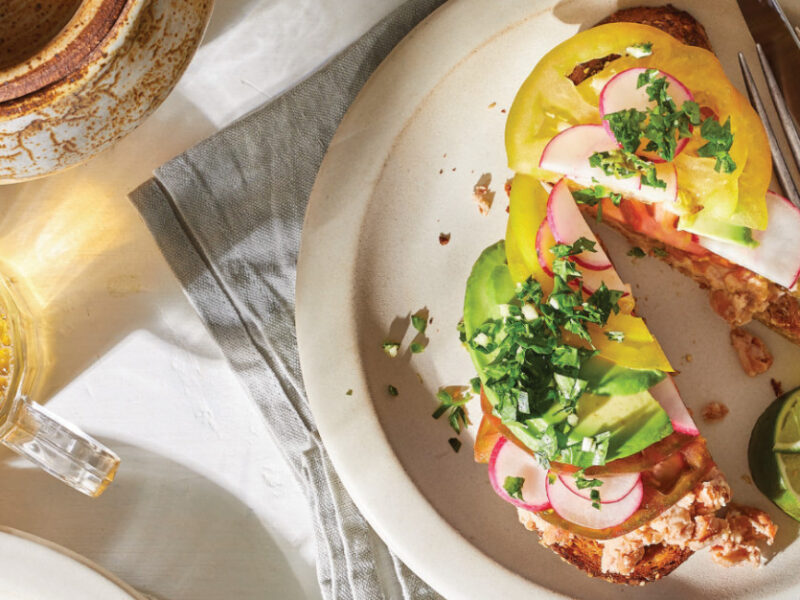 Avocado Toast with Tomato and Spicy Gremolata cut in half on a white plate with a silver knife and fork on the side