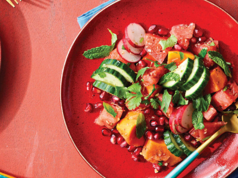 Tropical Fruit Salad with Ginger-Lime Dressing on a red plate sitting on a dusky pink background