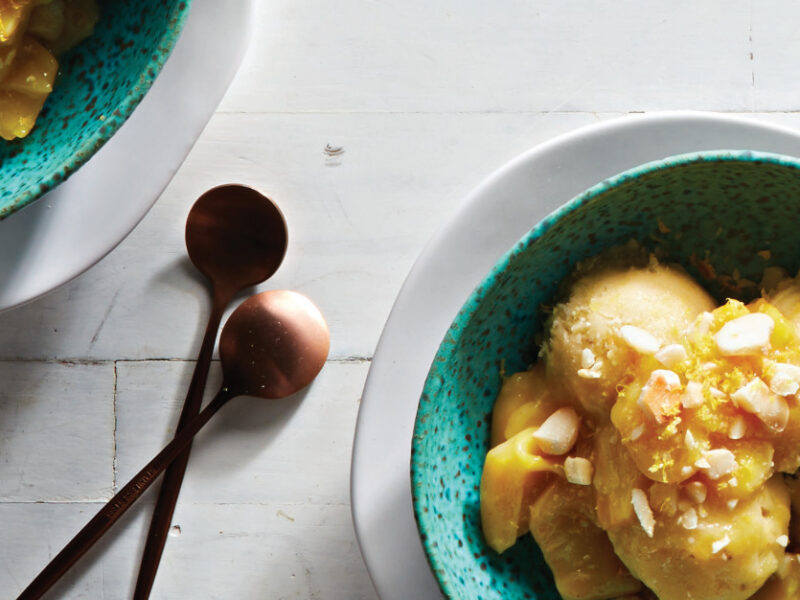 Two bowls of Dairy-Free Jackfruit Ice Cream in a specked green bowl nested on a white plate on a white countertop next to two small copper spoon