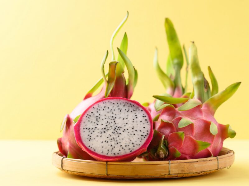 Halved fresh dragon fruit in a bamboo basket on yellow background
