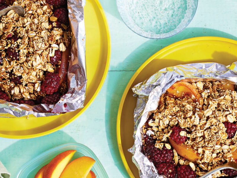 Two Foil-Roasted Blackberry Peach Crisps in tin foil on a yellow plate on a pale blue background