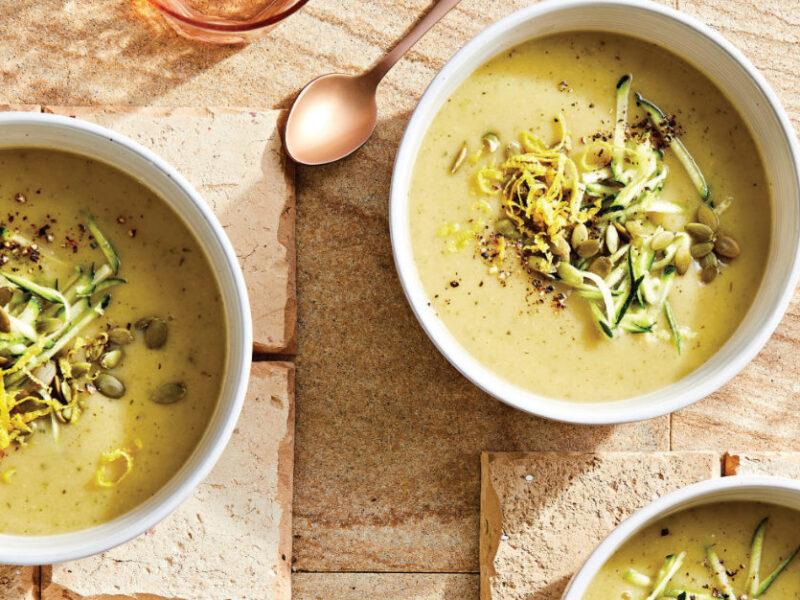 Two white bowls of Creamy Zucchini and Potato Soup with Lemon garnished with lemon zest, pepitas, and grated zucchini