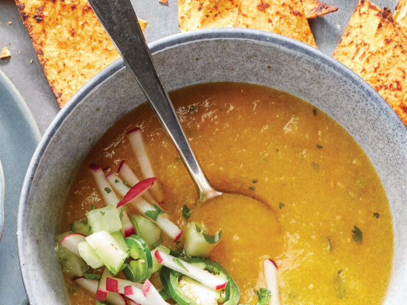 Yellow Tomato and Cucumber Gazpacho in a pale blue ceramic bowl with a handful of Chili-Lime Chips scattered around it