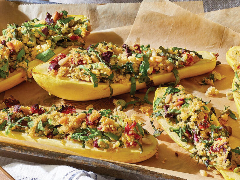 Stuffed Summer Squash with Quinoa, Chard, and Sun-Dried Tomatoes on a baking-paper lined baking tray held by two hands