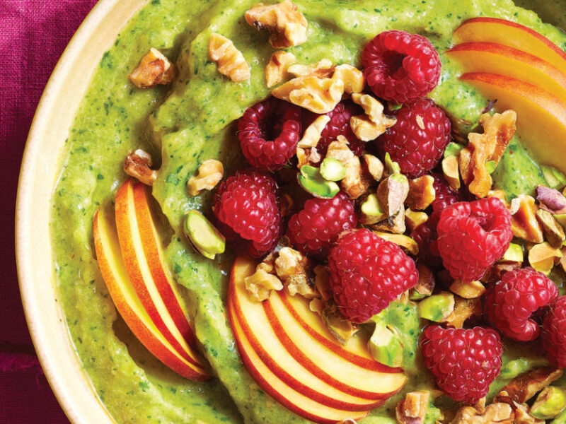 Close-up shot of Arugula and Peach Smoothie Bowl topped with sliced peaches, fresh raspberries and chopped walnuts and pistachios