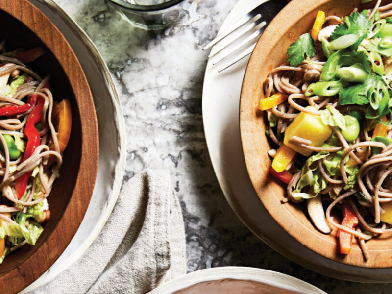 Two bowls of Spicy Cold Noodle Salad with Pineapple, Bell Pepper, and Soy-Lime Dressing in wooden bowls, each sitting on a white dinner late