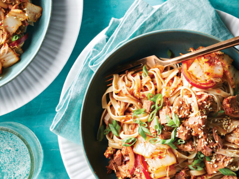 Vegan Bulgogi Noodles with Jackfruit Kimchi in a blue ceramic bowl on a pale blue napkin on a white plate with a fork sitting in the dish