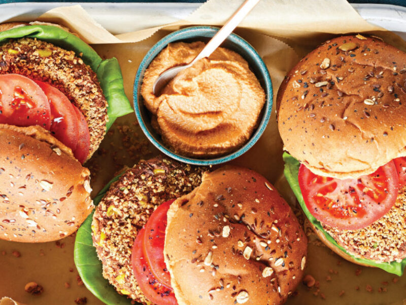 Three Chipotle-Lime Black Bean and Jackfruit Burgers in a white enamel pan with a small pot of chipotle-lime sauce.