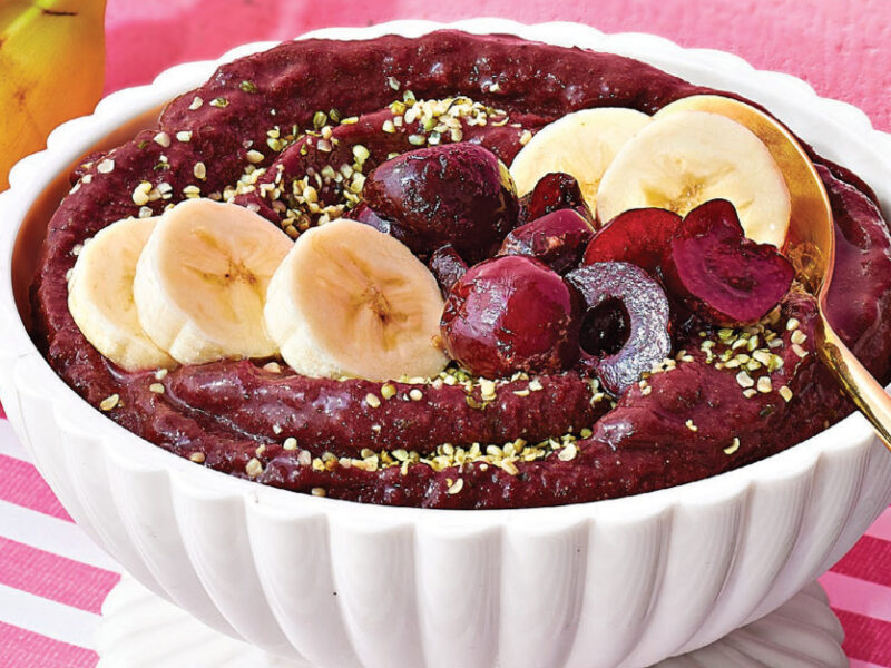 Cherry and Acai Smoothie in a white bowl on a pink and white striped tablecloth next to a couple of bananas