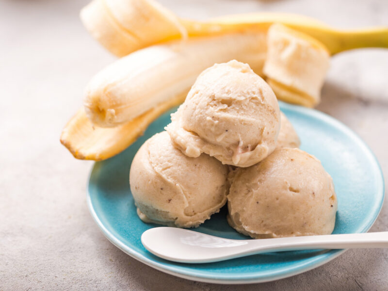 three scoops of nice cream (ice cream made from frozen bananas) on a plate with a spoon, with a banana visible in the background